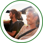 A couple smile as they drive a convertible along a bright coast. 